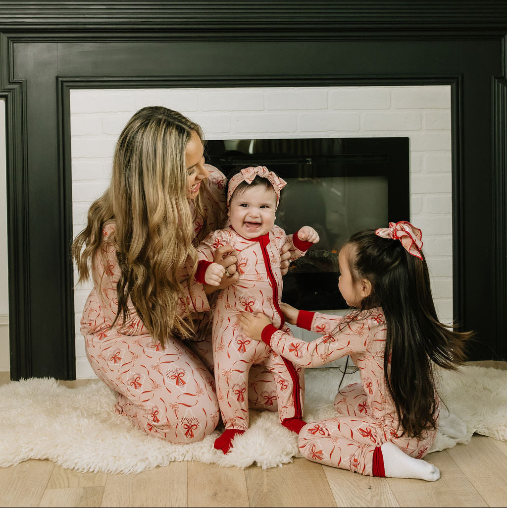 Girls wearing matching Candy Cane Coquette bow hair clips and holiday outfits while sitting with their mother by a fireplace.