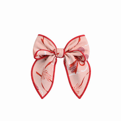 A pink hair bow accessory with a red patterned silk-like fabric and a red stitched border, shown against a plain white background.