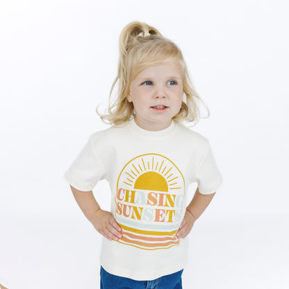 Child wearing a white t-shirt with 'Chasing Sunset' design on a white background