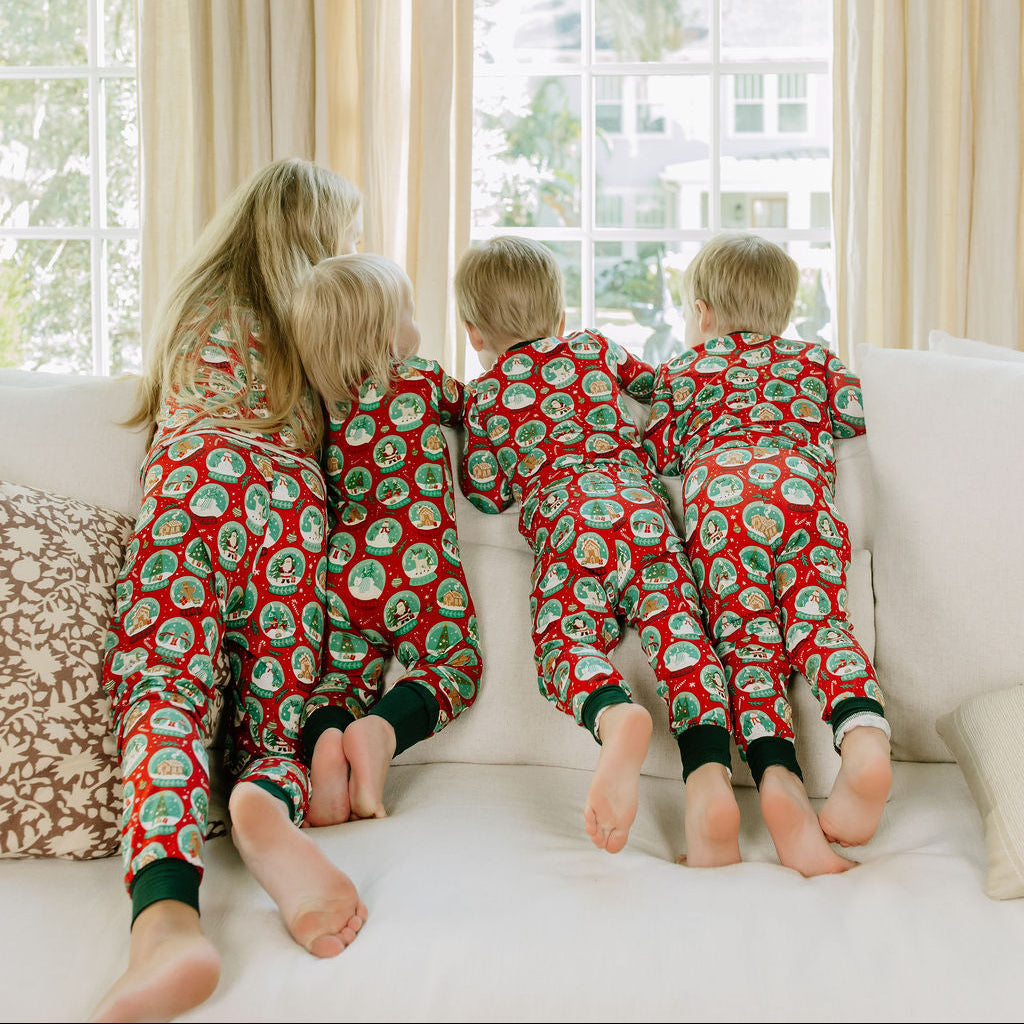 Children wearing matching Christmas bamboo pajamas while standing together beside a Christmas tree.