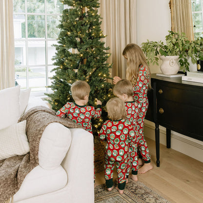 Two children wearing matching Christmas bamboo pajamas while standing together beside a Christmas tree.
