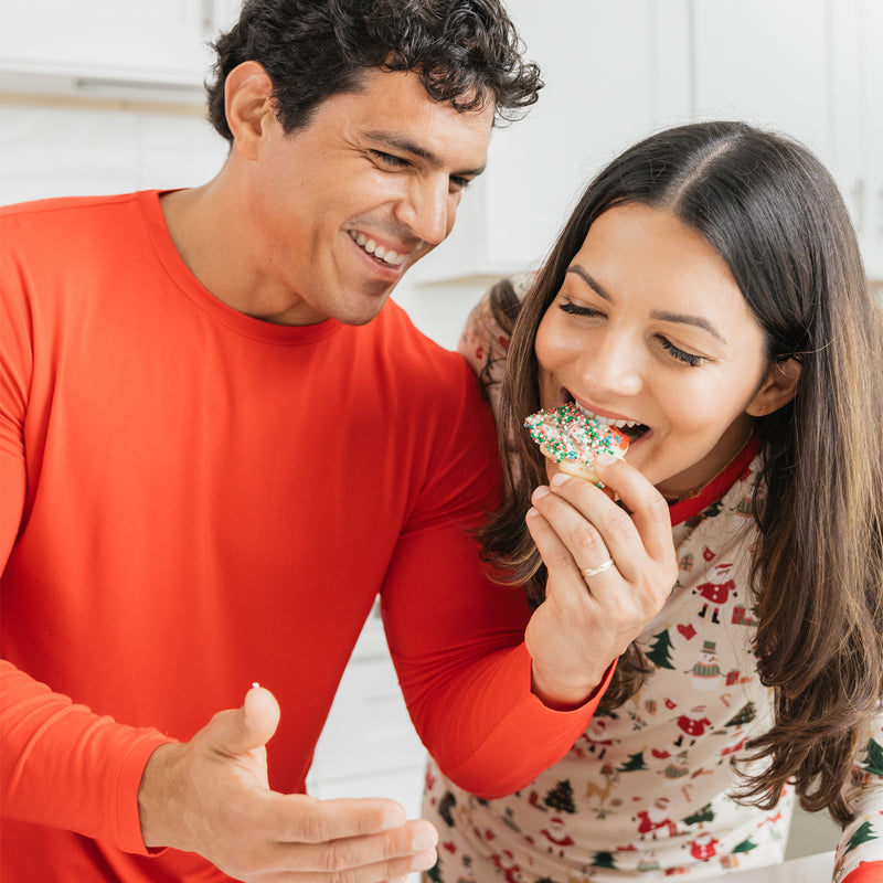 Couple wearing Christmas Red bamboo top and Cozy Christmas pajamas decorate cookies, enjoying cozy holiday moments.
