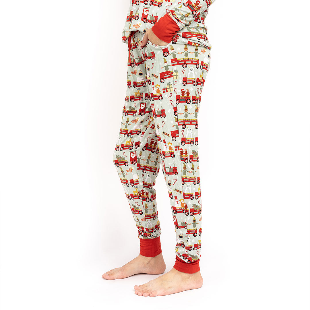 woman poses with her hands in her pockets of the "christmas train" women's jogger pajama pants. the "christmas train" pattern has various winter character that stand/ride on a red train. these characters include: santa, santa's elves, raindeers, yeti monsters, gingerbreads, reindeer, christmas trees, candy canes, presents, and snowflakes. 