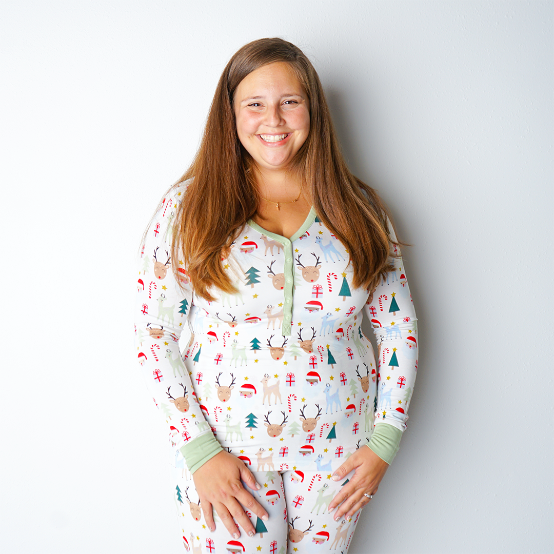 woman poses in the "Santa and friends" women's top. the "Santa and friends" print is a Christmas themed pattern mixed with Santa heads, candy canes, reindeer, Christmas trees, Rudolph heads, and gold stars. this is all on a white background. 