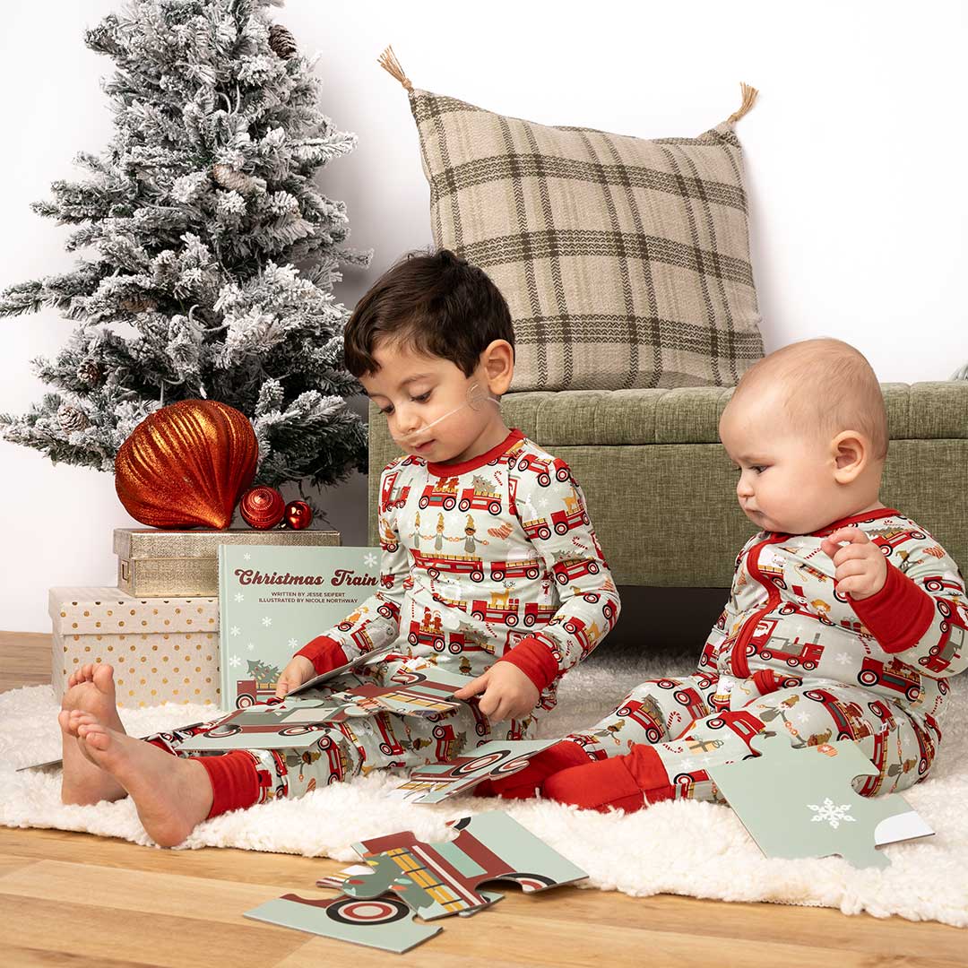 2 little boys wear matching "christmas train" pajamas in the convertible and the matching pajama set. they play with the "christmas train" puzzle. 