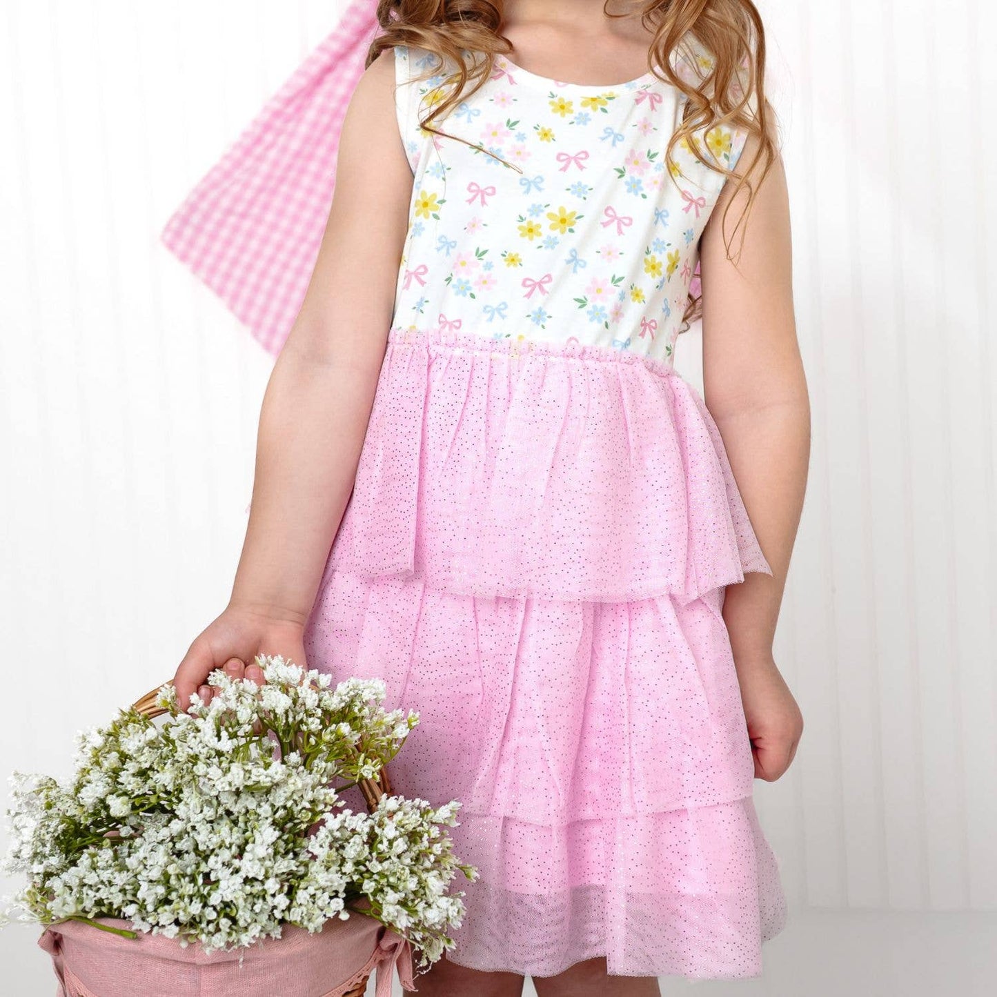 Child wearing a white floral top and pink skirt holding flowers against a white background