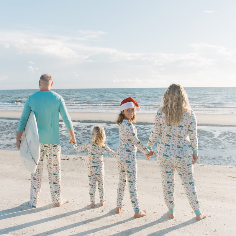 Family of four in matching pajamas on a beach with a surfboard.