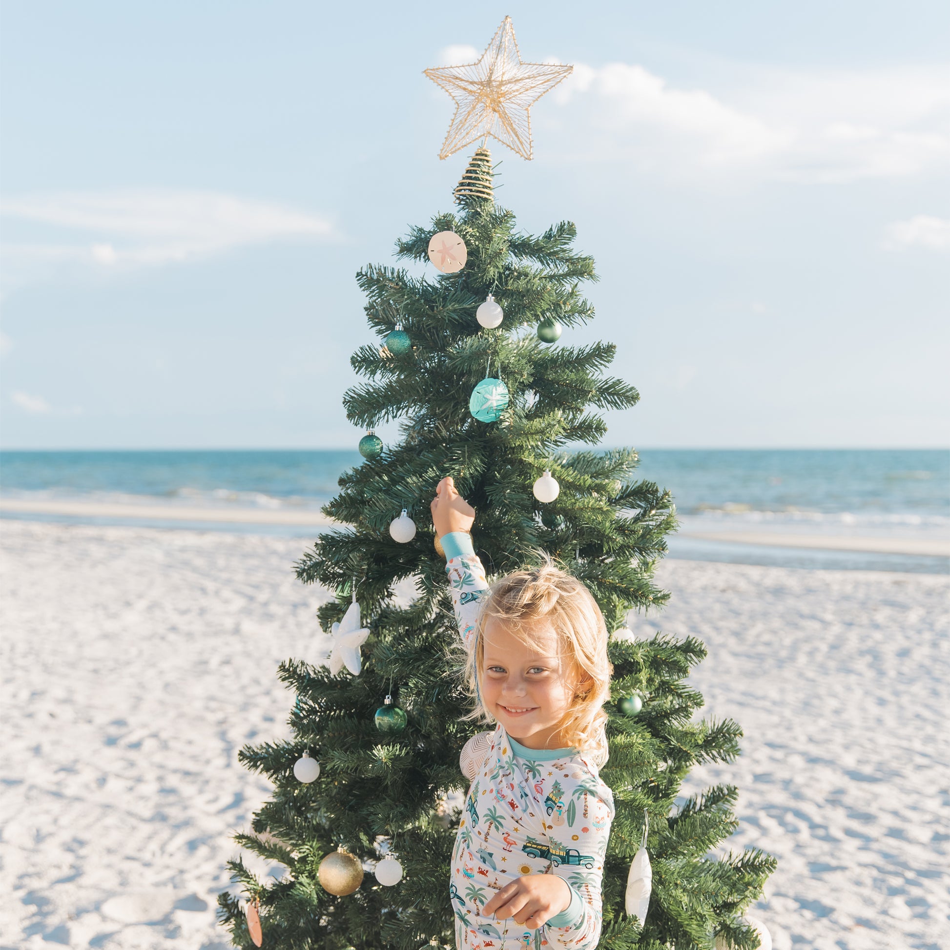 Child decorating a Christmas tree on a beach with a star ornament