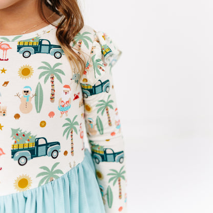 Child wearing a colorful outfit with palm trees, trucks, and other patterns on a white background