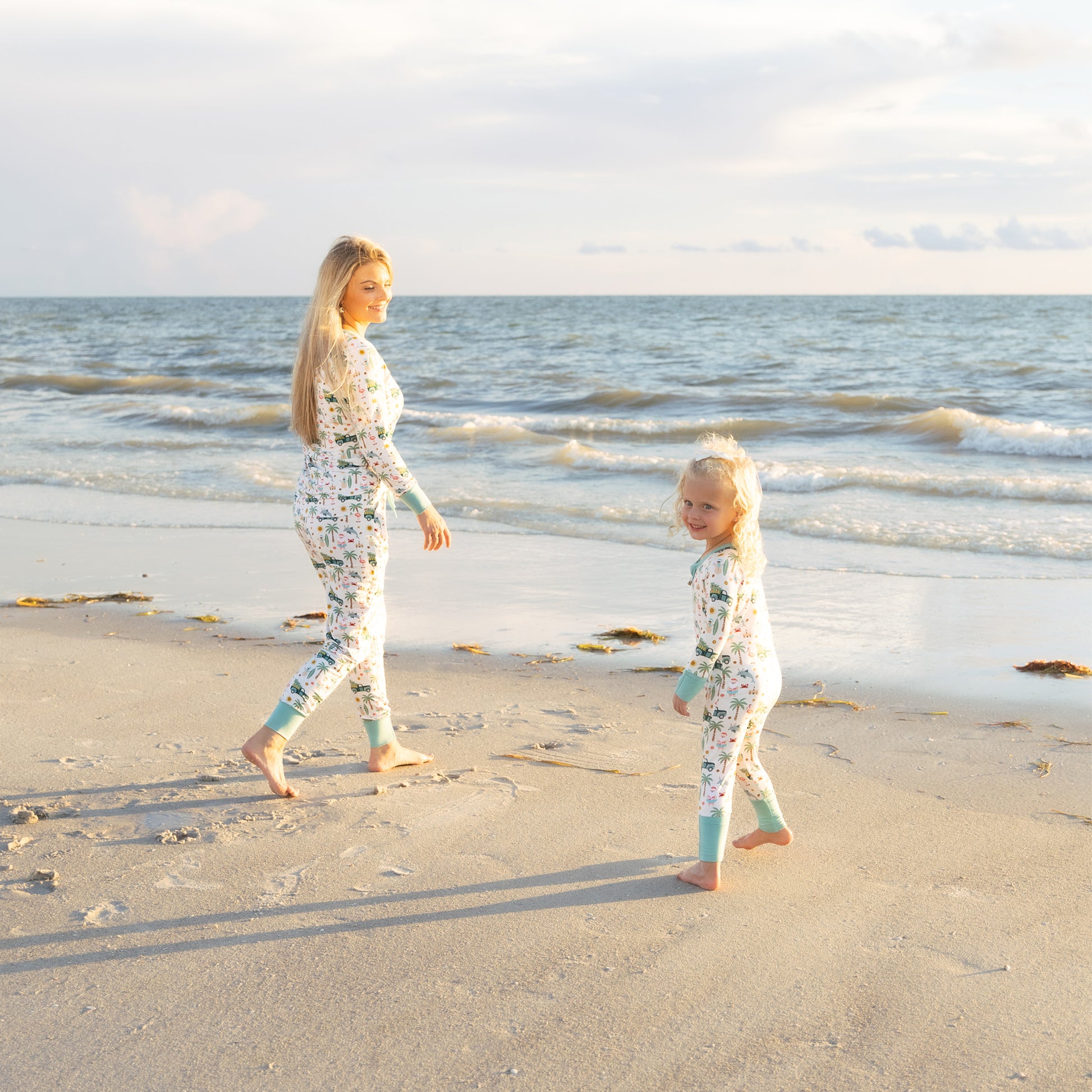 Woman and child walking on a beach wearing matching outfits.