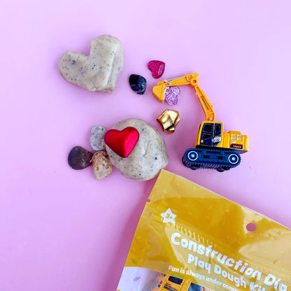 Construction-themed play dough kit with toys on a pink background