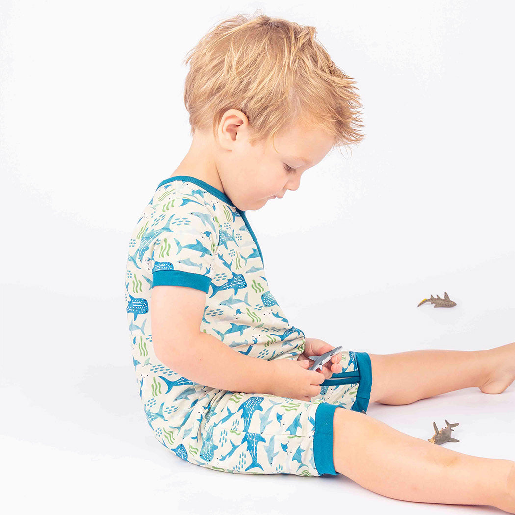 Little boy sitting while wearing our Shark Friends Shortie Romper.