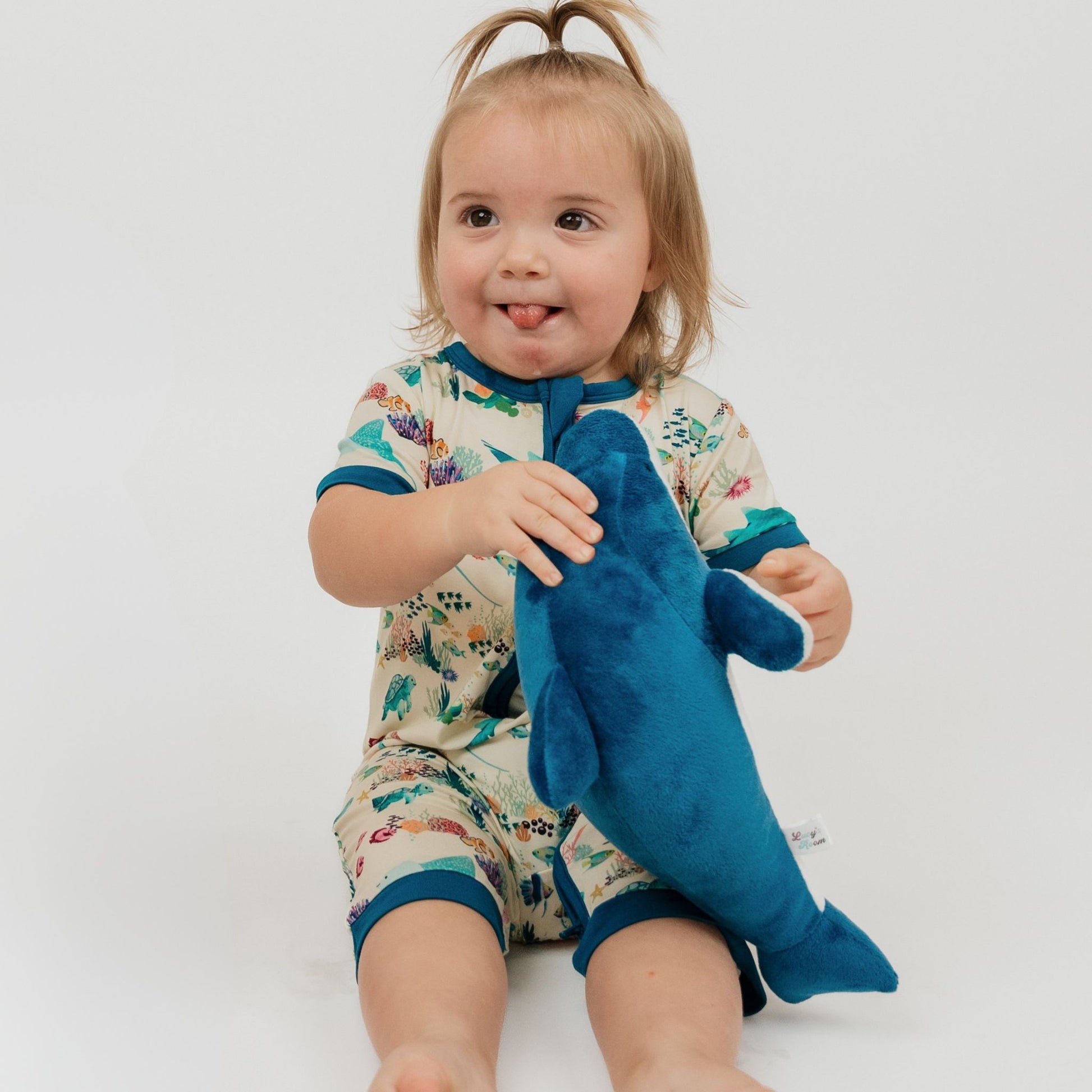 Child wearing a colorful onesie holding a blue shark toy on a white background