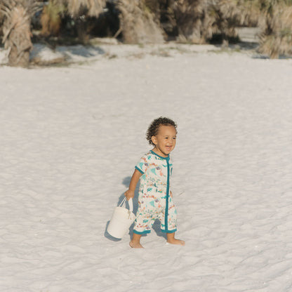 Baby boy smiling while walking with our Emerson and Friends Coral Reef Bamboo Baby Shortie Romper, a soft and breathable summer outfit featuring an ocean-inspired print with sharks, sea turtles, and coral, designed for all-day comfort with an easy zip closure.