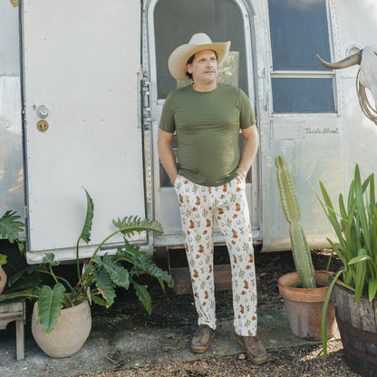 Man modeling Cowboy Christmas Bamboo Men's Lounge Pants featuring festive Western holiday print, styled with a green T-shirt and cowboy hat.