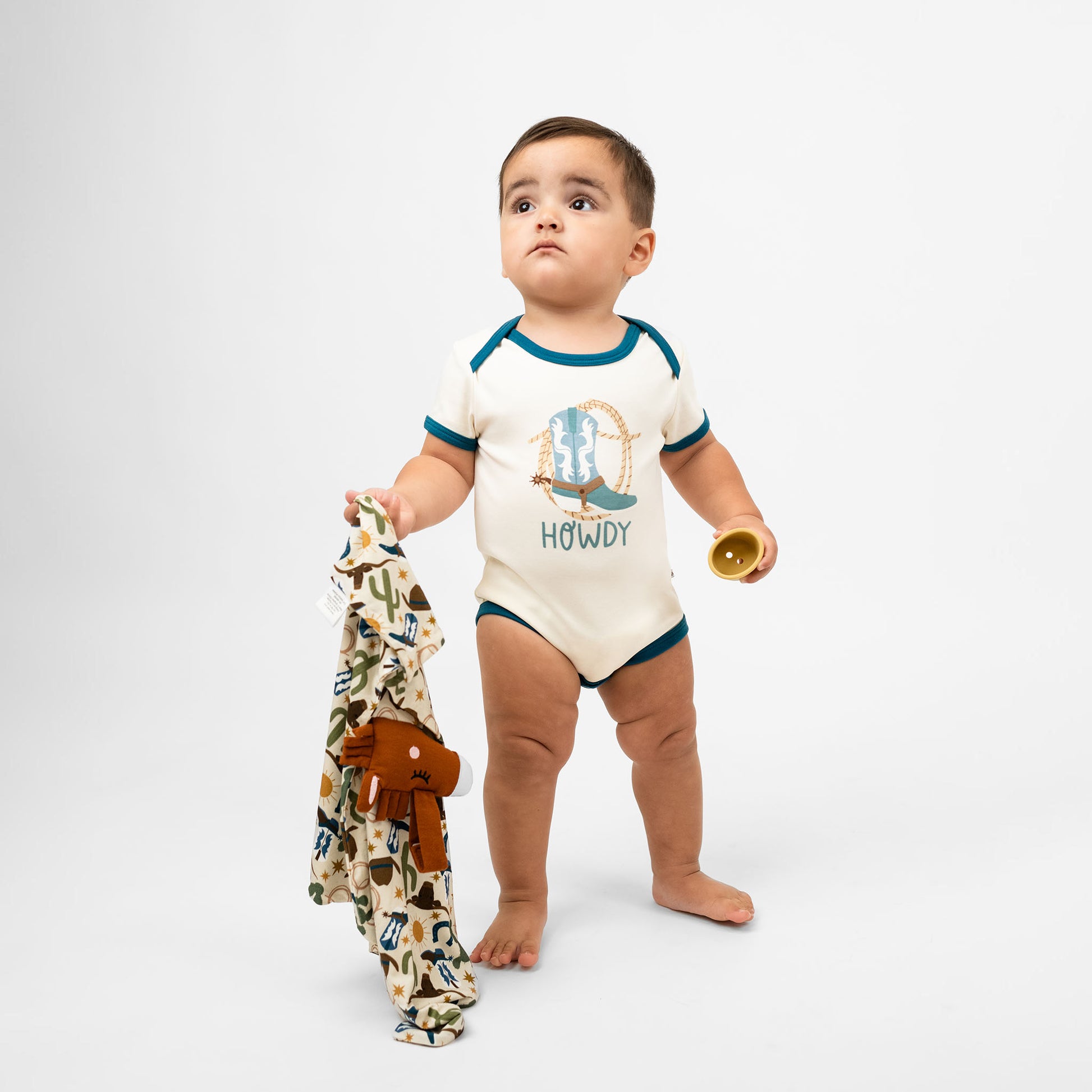 Baby boy wearing our Howdy cotton onesie featuring the word "Howdy" in playful, blue letters, perfect for a western outfit while holding our Howdy Lovey