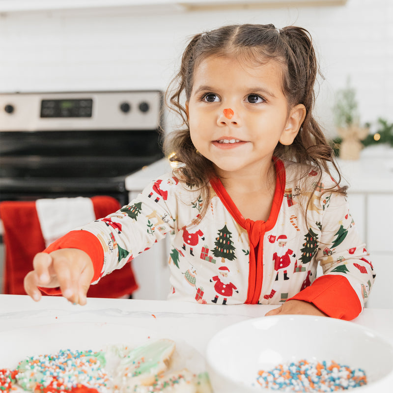 Toddler girl in Cozy Christmas bamboo pajamas decorating holiday cookies in a kitchen – soft and breathable sleepwear for kids.