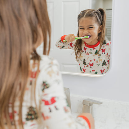 Girl wearing Cozy Christmas bamboo pajamas smiles in the mirror, showing off the festive holiday print with red trim.