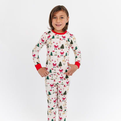 Child standing in studio wearing Cozy Christmas bamboo pajamas, featuring Santa and tree print with bright red cuffs.