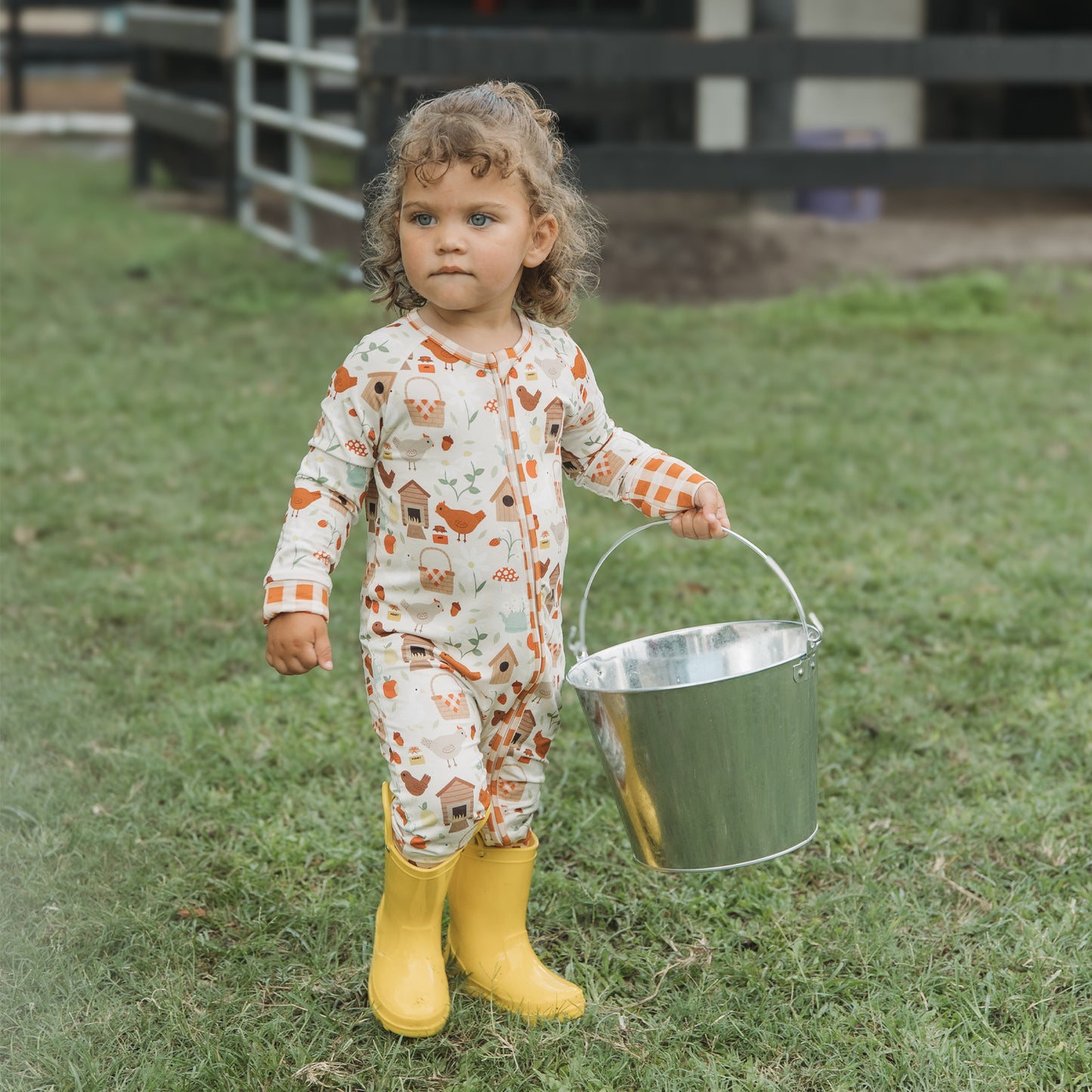 Toddler in Cozy Cottage bamboo zipper pajamas with yellow boots and farm bucket.