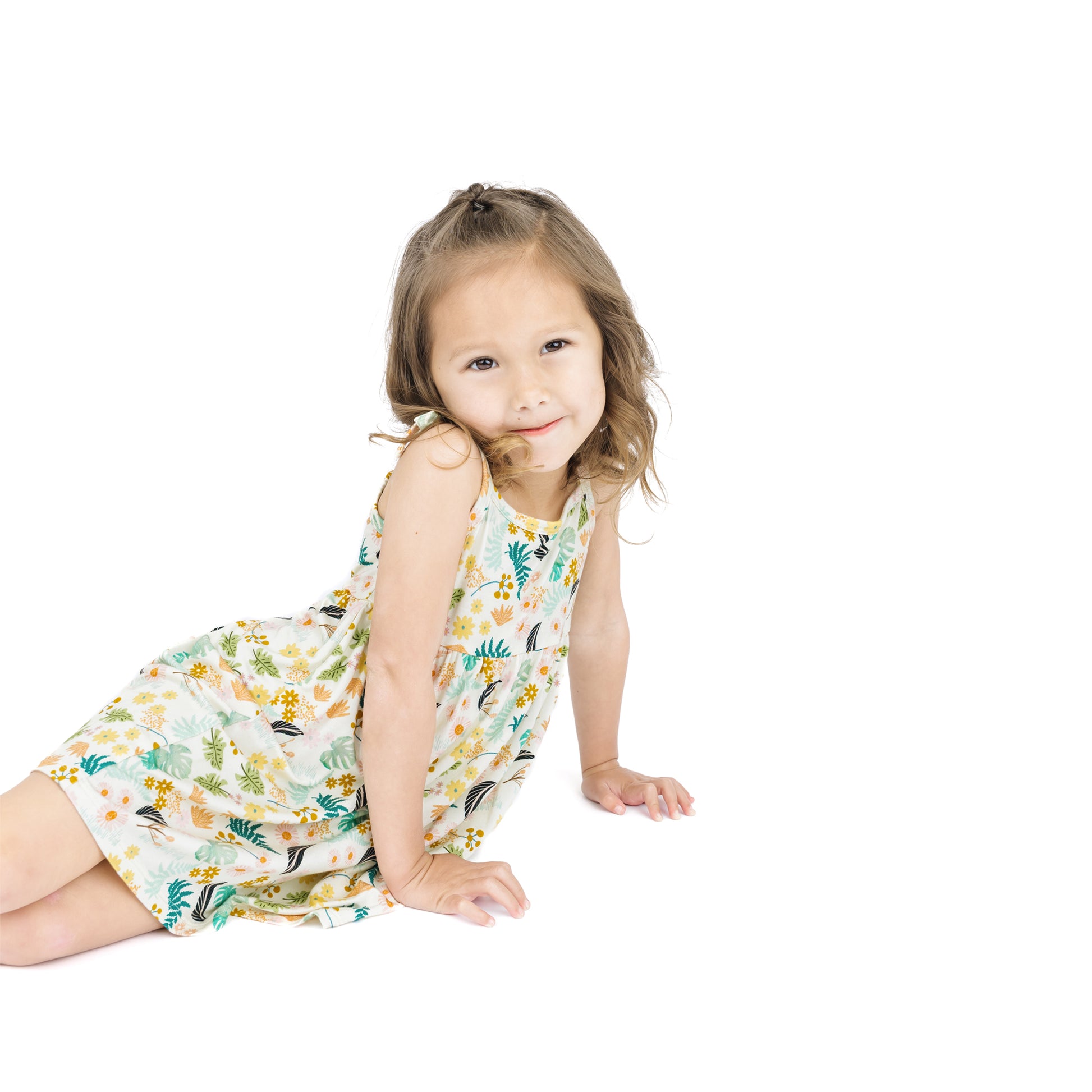 Young girl sitting in the Tropical Blooms sundress, demonstrating the moisture-wicking fabric's suitability for warm weather.