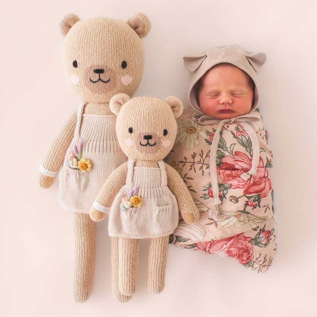 Two knitted teddy bears and a baby wrapped in a floral blanket on a light pink background