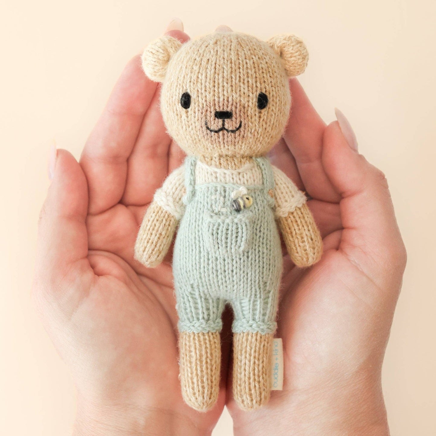 Knitted teddy bear toy held in hands against a plain background