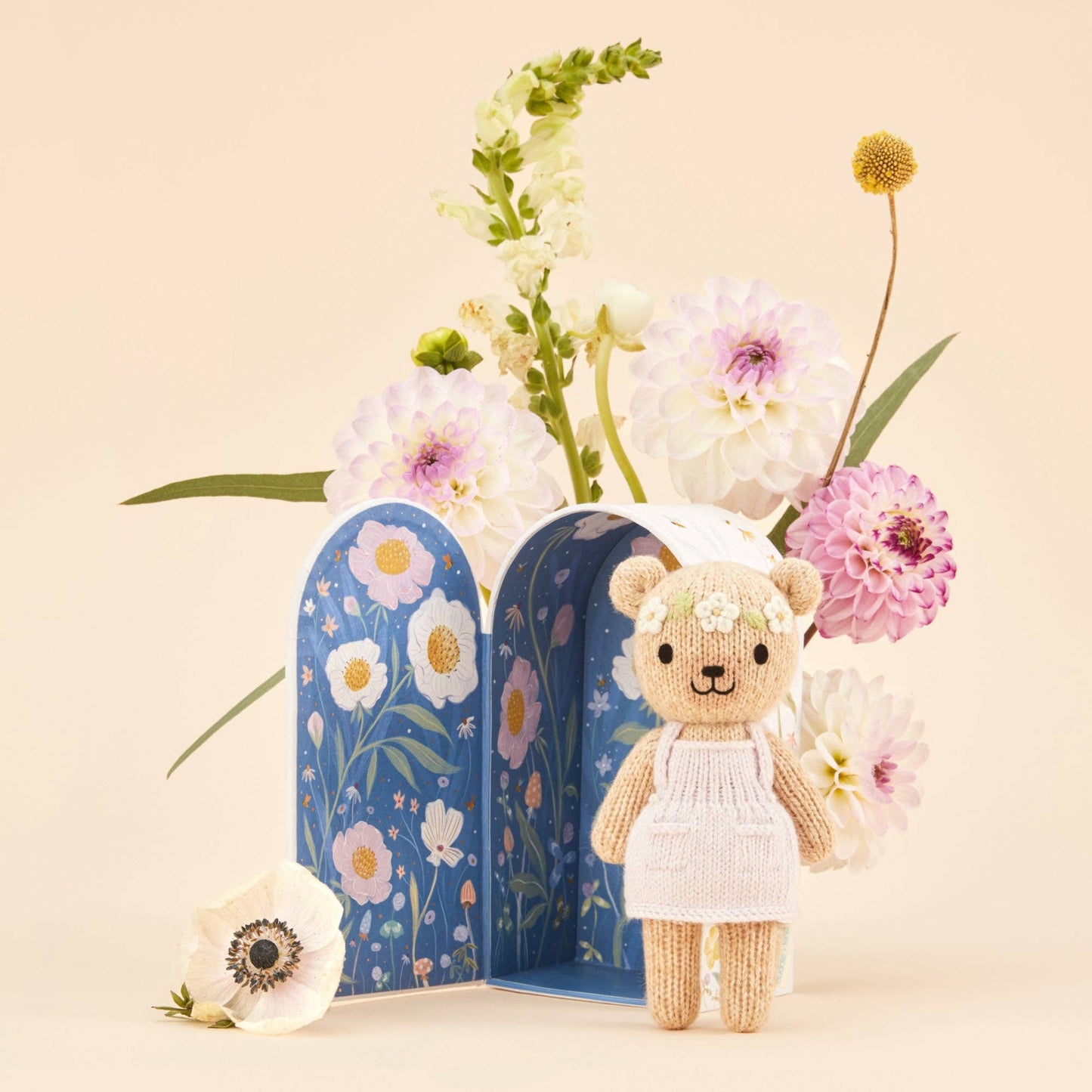Small teddy bear in a white dress standing next to floral bookends with flowers on a beige background