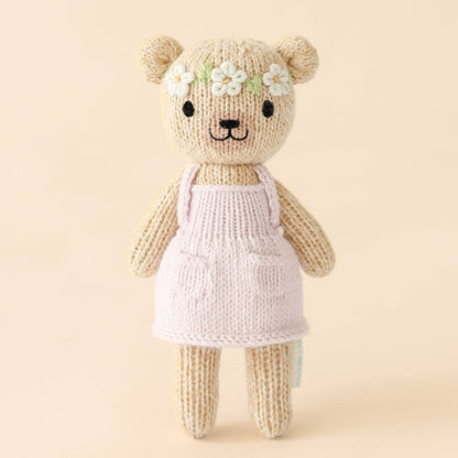 Knitted teddy bear with a pink dress on a beige background