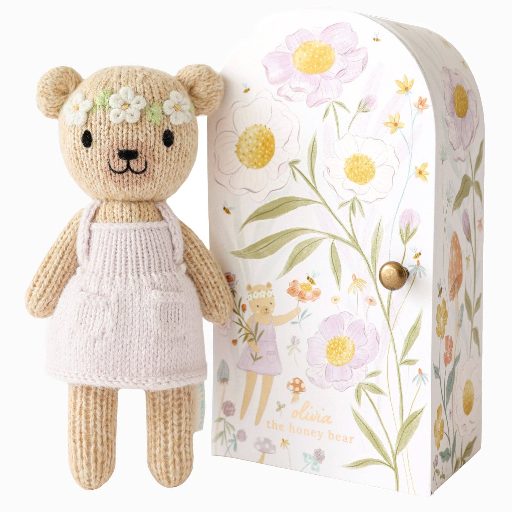 Knitted teddy bear with a floral headband next to a decorative box with floral patterns.