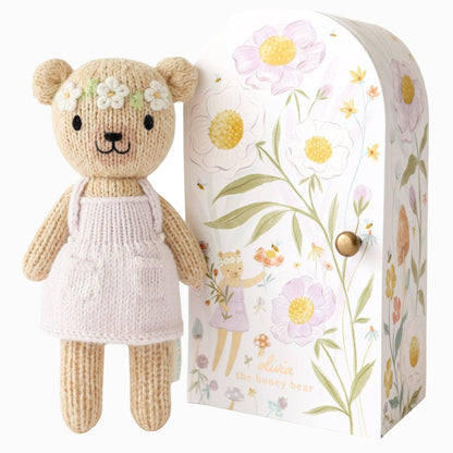 Knitted teddy bear with a floral headband next to a decorative box with floral patterns.