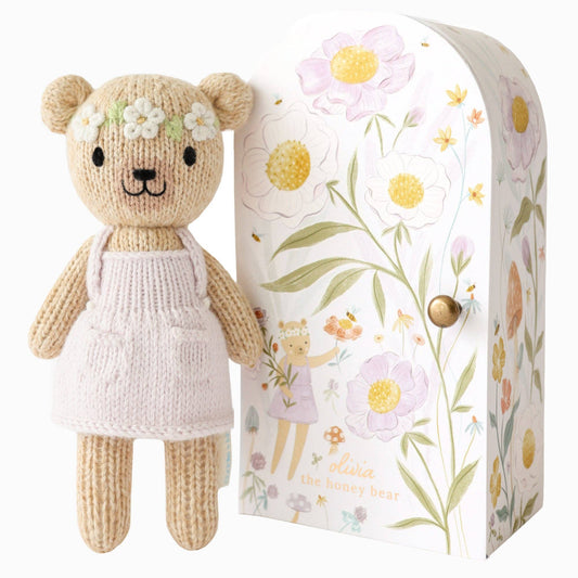 Knitted teddy bear with a floral headband next to a decorative box with floral patterns.