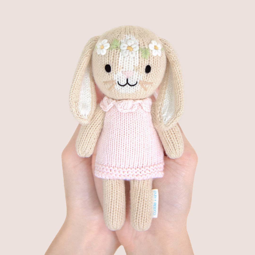 Knitted bunny toy with a pink dress held in a hand against a plain background
