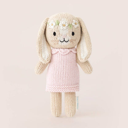 Knitted bunny toy with a pink dress on a light beige background