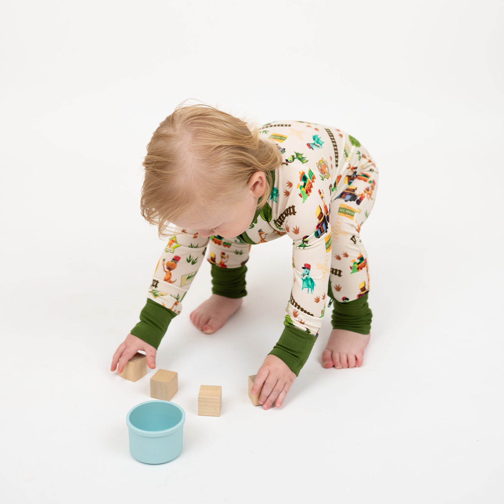 Toddler with our Emerson and Friends All Aboard the Dino Train bamboo convertible baby pajamas with green trim, double zipper, and colorful orange, blue, and green dinosaurs on train tracks with "Dino Train" print.
