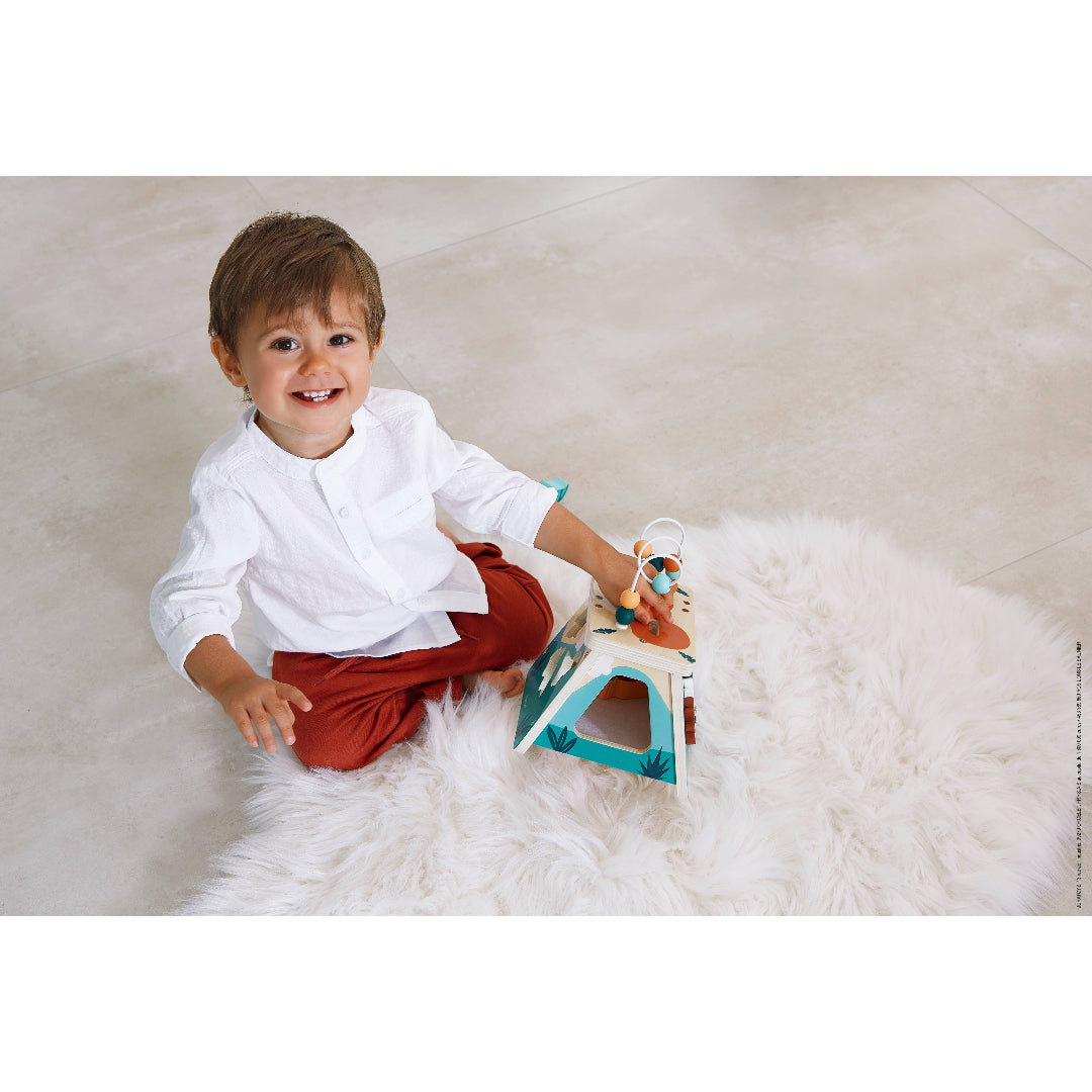 little boy playing with volcano shaped wooden learning toy with multiple activities including a shape sorter and bead maze on top