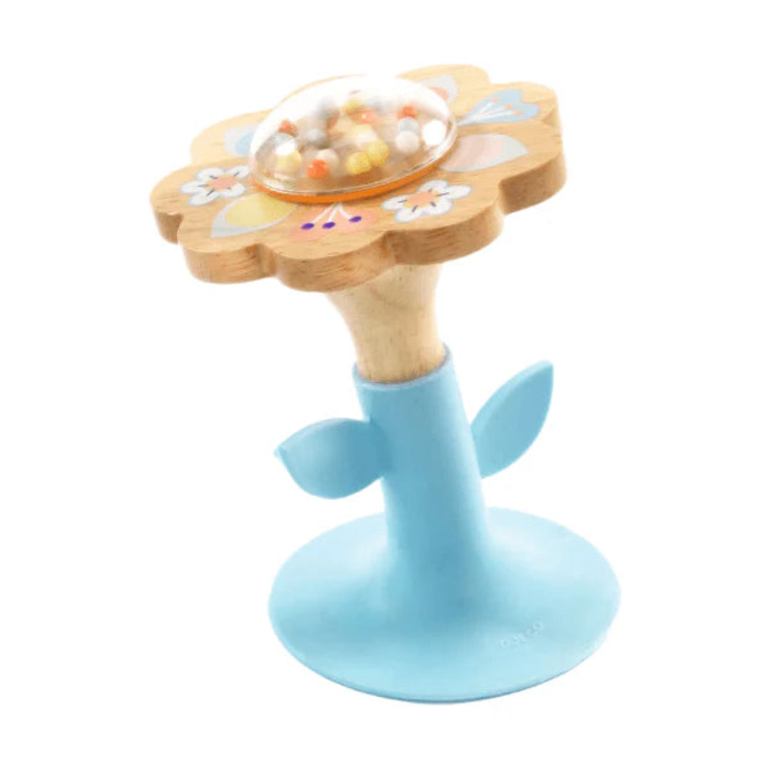a suction cup baby rattle that is shaped like a flower with a wooden top, and a clear center dome with beads inside of it, and the base is blue silicone that suctions to the table