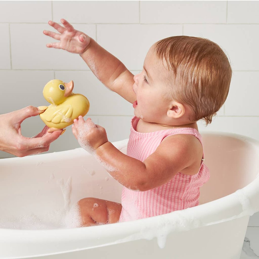 baby girl in a swimsuit in a bath tub grabbing for a yellow rubber duck