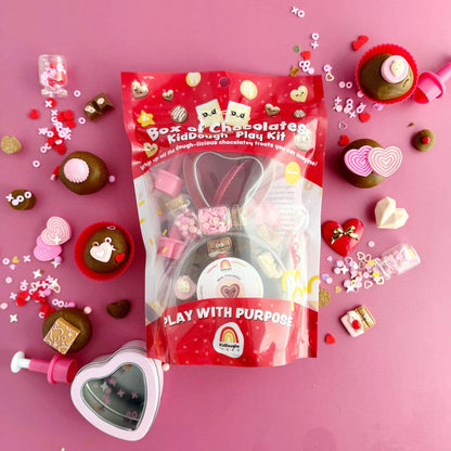 Red packaging of a play kit with various small toys and items on a pink background