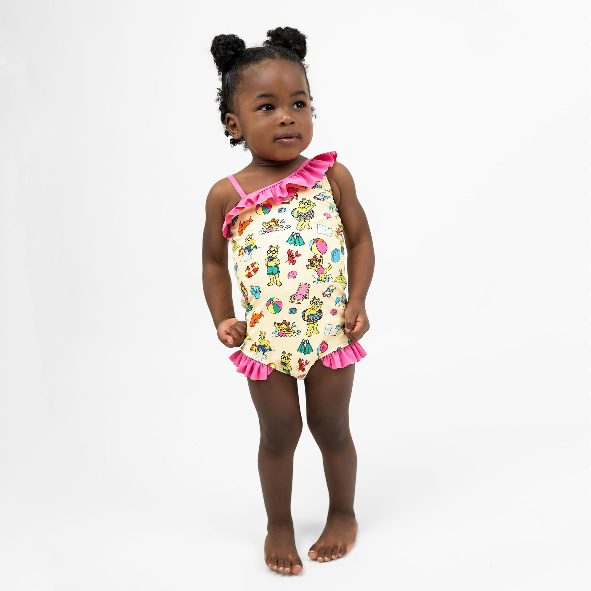 Toddler wearing our Emerson and Friends Arthur's Family Vacation Girls One-Piece Swimsuit, featuring a playful beach-themed print with Arthur and friends, ruffle details on the shoulder and legs, and a soft, stretchy fabric for a fun and comfortable swimwear option.
