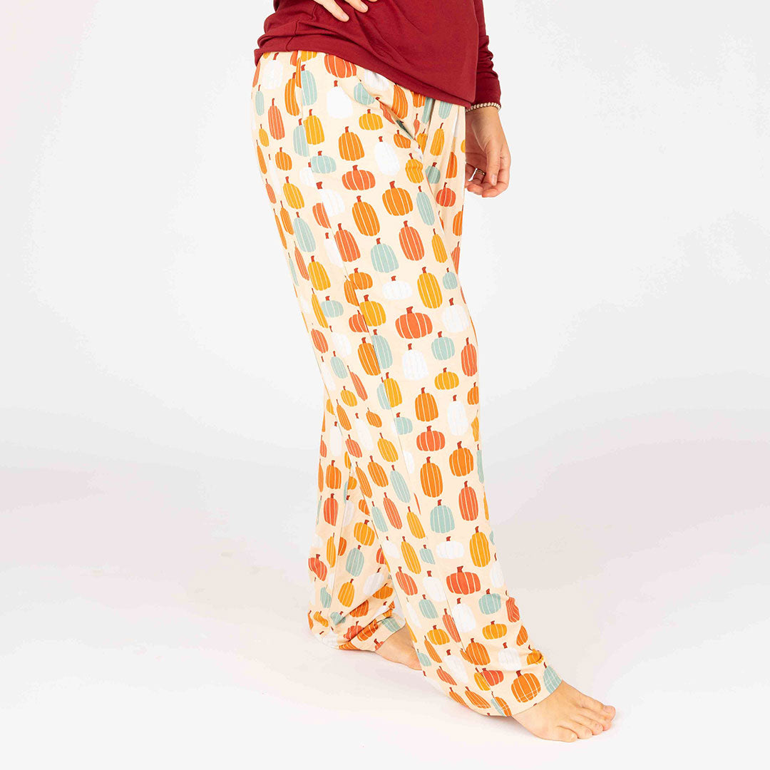 someone poses in the "pumpkin patch" relaxed pants. the 'pumpkin patch" print is a mix of boho styled and colored pumpkins. you can see white, blue, orange, and red pumpkins in.different shapes and sizes. this is all on a pastel orange background. 