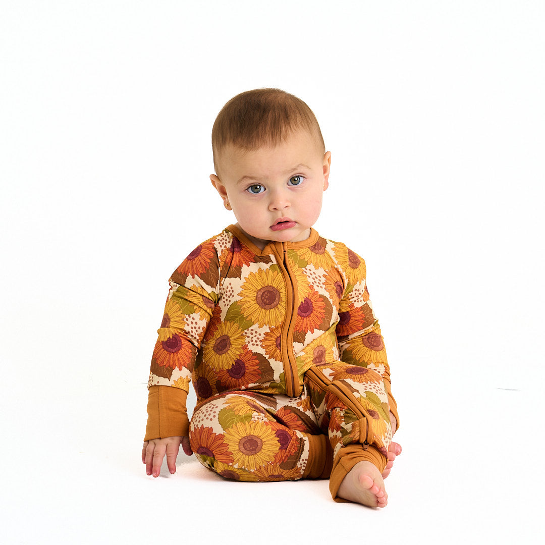 small baby stares into the camera in the "sunflower" convertible. the "sunflowers" print is a sunflower floral design. it has a variety of yellow, orange, and red sunflowers, mixed into green leaves. 