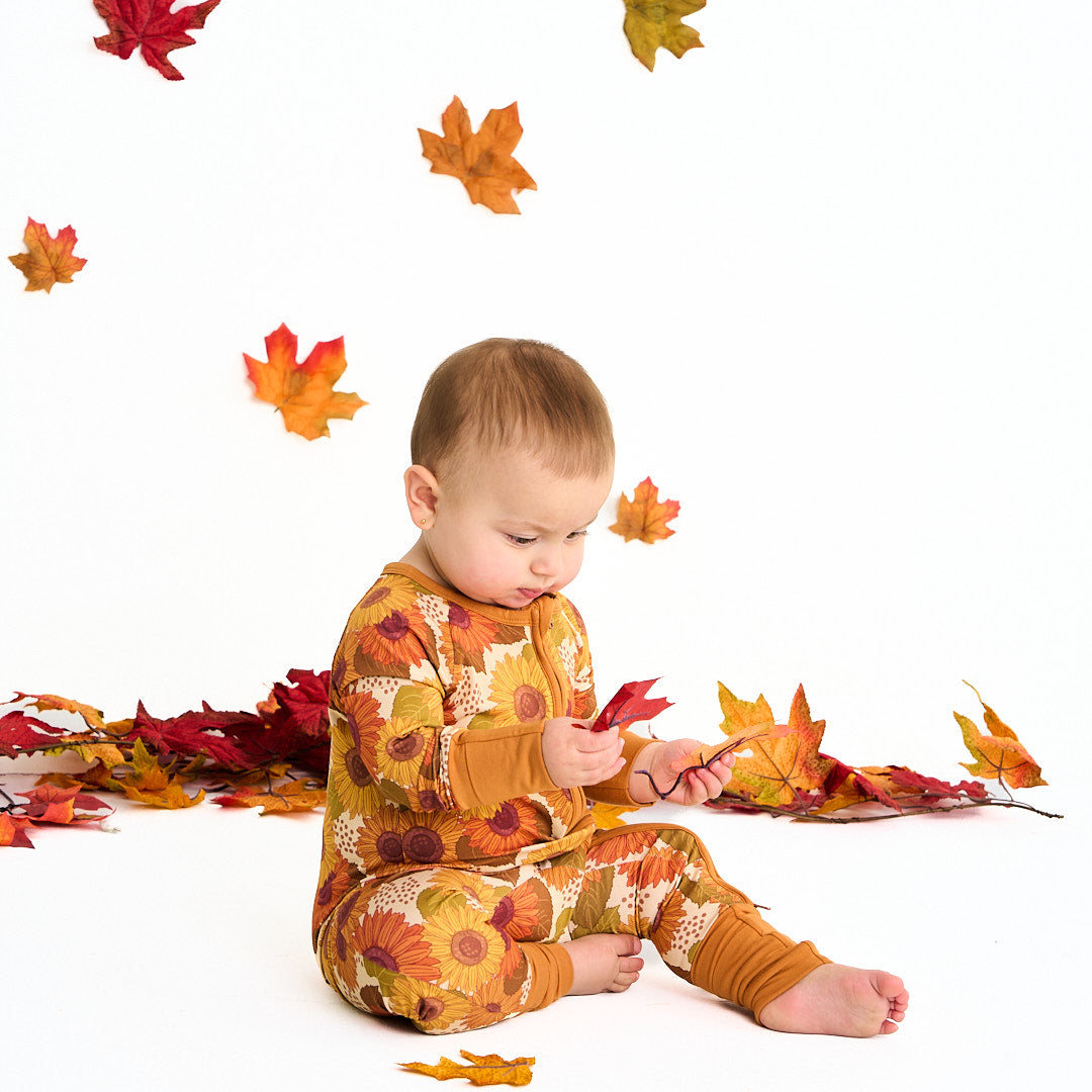 small baby holds and stares at a fall leaf. the baby wears the "sunflower" convertible. the "sunflowers" print is a sunflower floral design. it has a variety of yellow, orange, and red sunflowers, mixed into green leaves. 