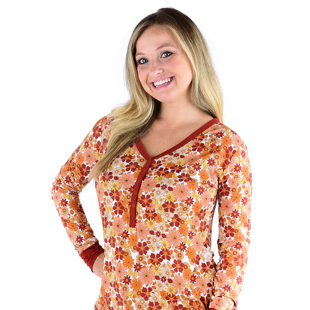 woman smiles and poses with her hand on her hip. she wears the "fall floral" women's top. the "fall floral" print is a floral flowered print that is filled with fall colors and flowers. 