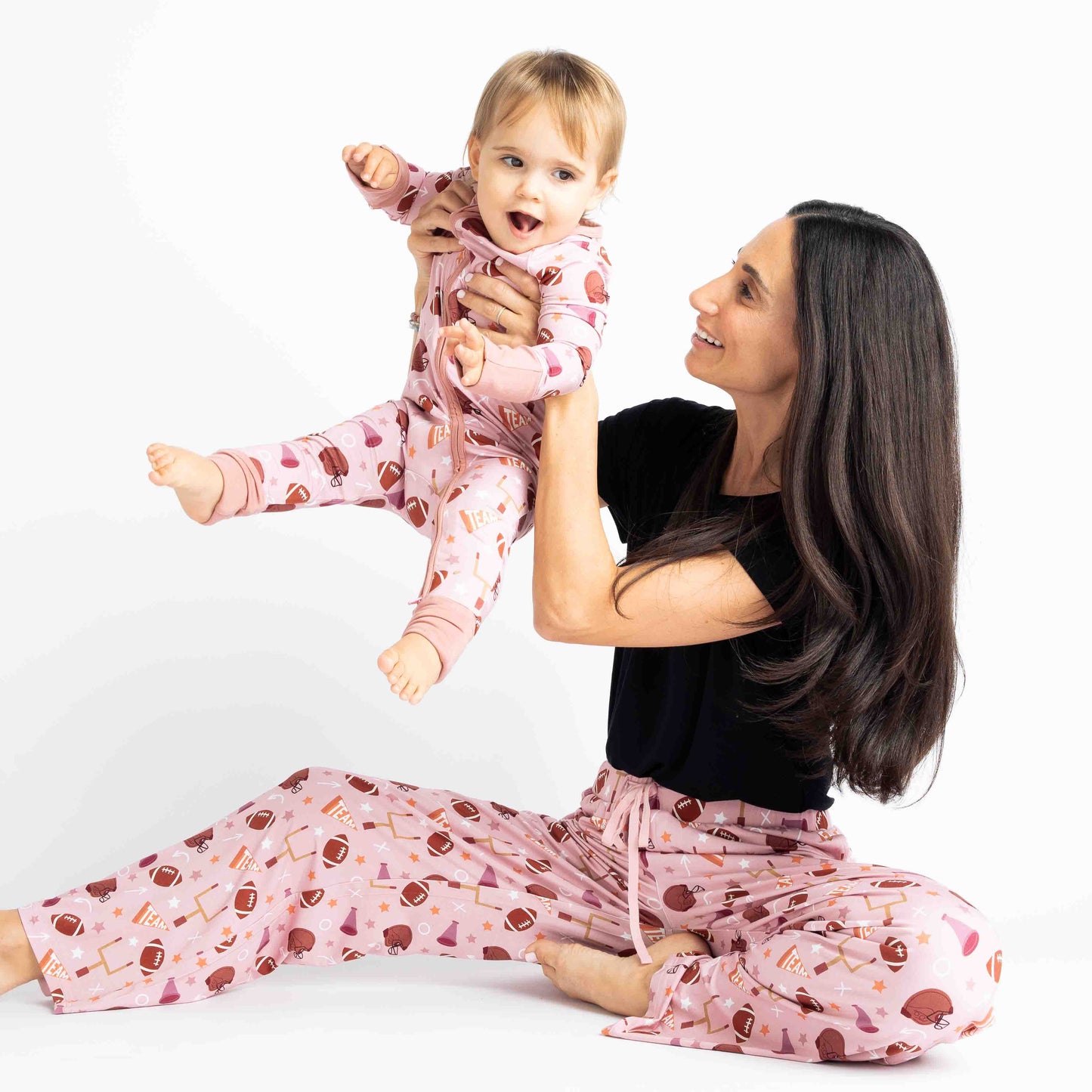 Mom holding baby girl in air while modeling  our pink football print called "Game Day" Featuring footballs, goal posts, stars and more!