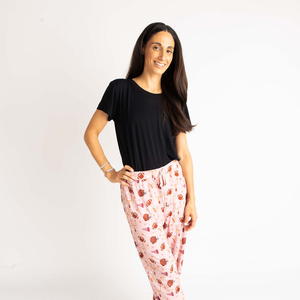 Mom standing with balck t-shirt on and lounge pantsmodeling our pink football print called "Game Day" Featuring footballs, goal posts, stars and more!