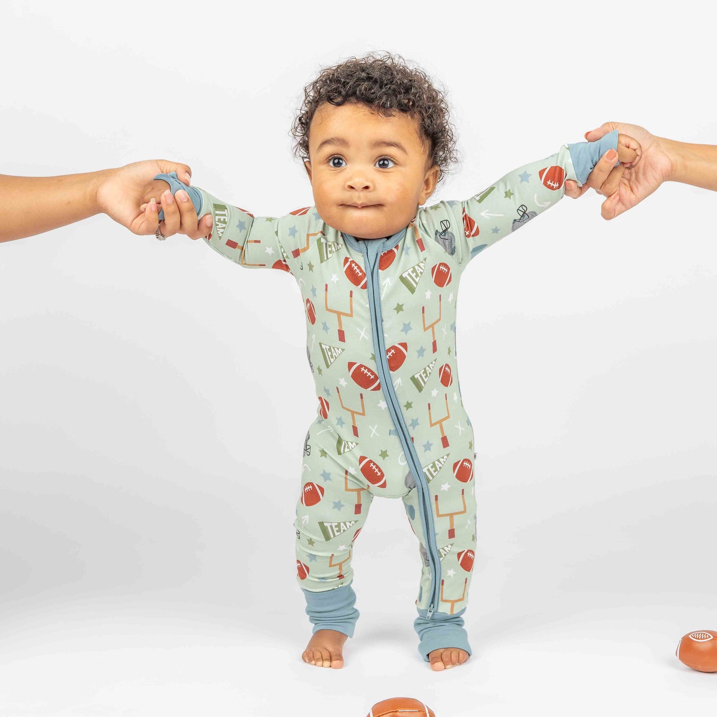 baby boy standing while modeling green football print called "Game Day" Featuring footballs, goal posts, stars and more! 