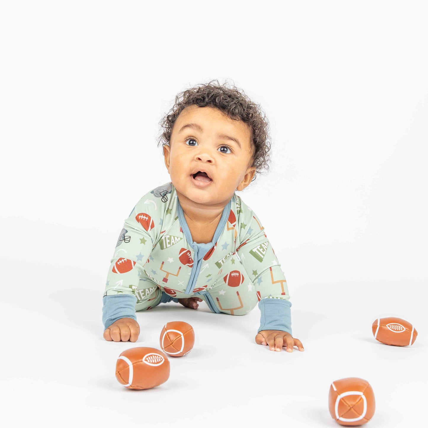 Baby boy crawling while modeling green football print called "Game Day" Featuring footballs, goal posts, stars and more! 