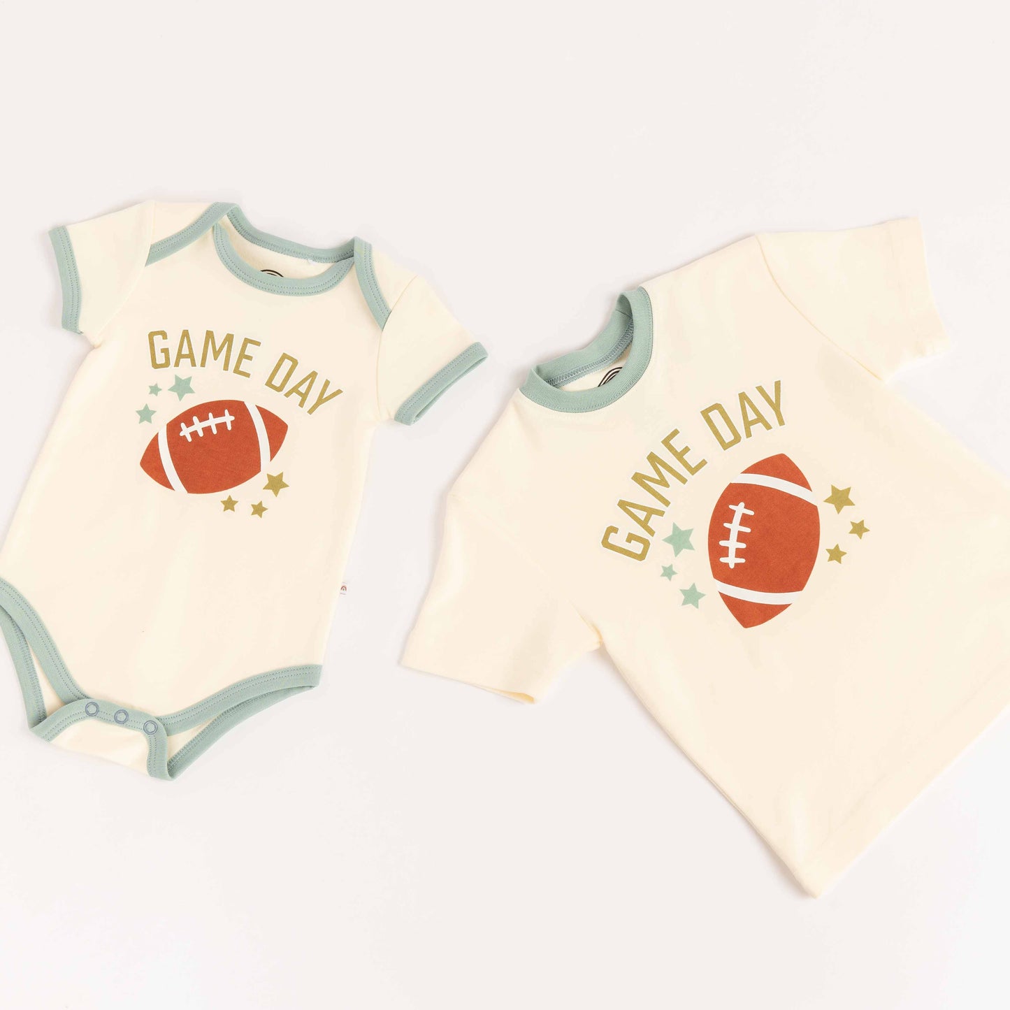 Flatlay of bamboo tee-shirt, and ba,boo onesie laying on white background. Both say "Game Day" with a football on them