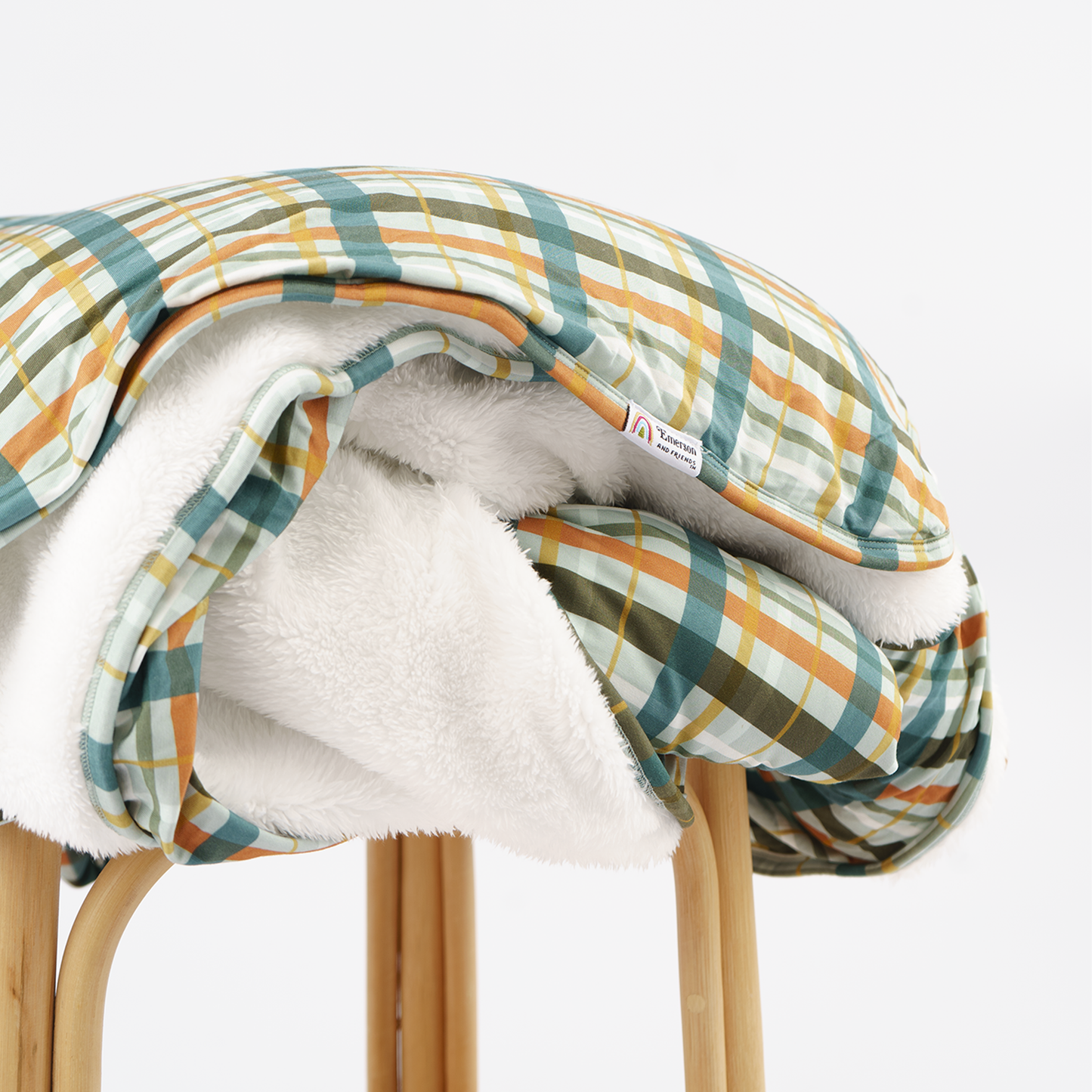 plaid blanket print with white fleece lining on rattan stool with white background.